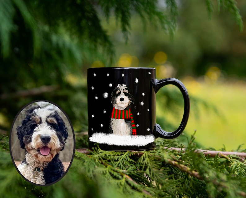May include: Black ceramic mug with a white dog wearing a red and green scarf in a snowy scene. The dog is a doodle breed with black and white fur.