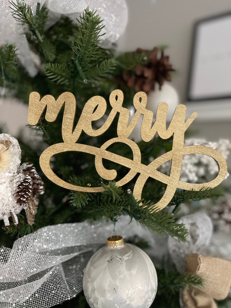 May include: Gold glitter "merry" sign hanging on a Christmas tree with white and gold ornaments.