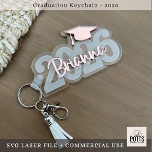 May include: A clear acrylic graduation keychain with the name "Brianna" in rose gold script, and the year "2026". The keychain includes a tassel and a graduation cap design. The text "Graduation Keychain - 2026" is at the top.