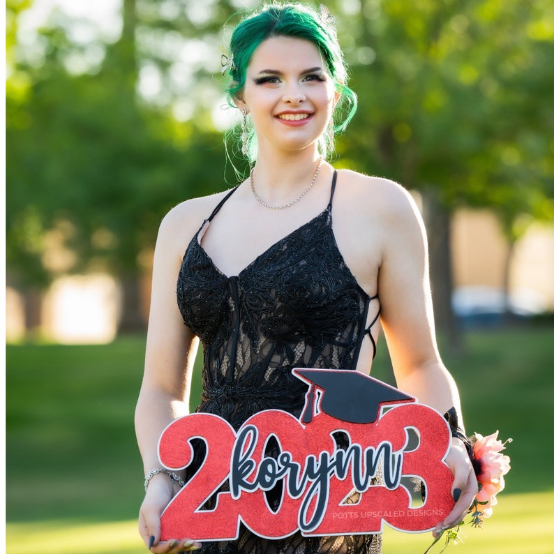 Senior picture of girl holding personalized deluxe graduation sign in school colors of silver black and red glitter