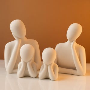 May include: A set of four white ceramic sculptures depicting abstract human figures. The figures are stylized and have simple, rounded features. They are arranged in a group, with two larger figures standing and two smaller figures sitting.