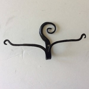 May include: Black metal wall hook with a decorative swirl design. The hook has two arms that extend out from the center.