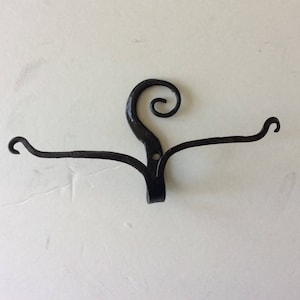 May include: Black metal wall hook with a decorative swirl design. The hook has two arms that extend out from the center.
