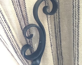 May include: Black metal curtain tieback with a decorative scroll design. The tieback is holding back a striped curtain.
