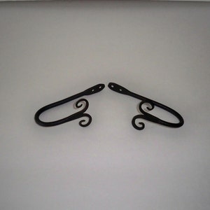 May include: A pair of black metal curtain tiebacks with a decorative swirl design.
