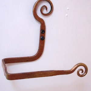 May include: A gold-colored metal toilet paper holder with a decorative scroll design on each end.