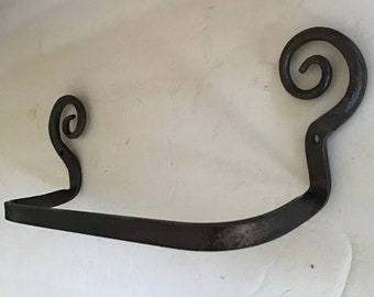 May include: Black metal towel rack with two decorative scroll ends. The rack is designed to hold a roll of paper towels.