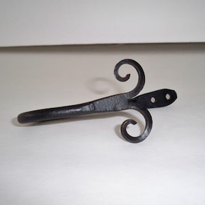 May include: Black metal curtain rod finial with a decorative scroll design. The finial has two holes for mounting.