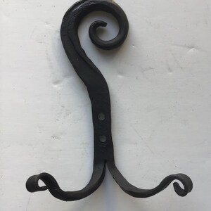 May include: Black metal double hook with a decorative swirl at the top. The hook is designed for hanging items on a wall.