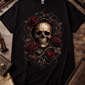 Op de afbeelding: Zwart t-shirt met een gedetailleerd schedelontwerp omringd door rode rozen en doornige ranken. De schedel heeft een verweerde uitstraling en de rozen zijn dieprood. Het ontwerp staat centraal op het shirt.