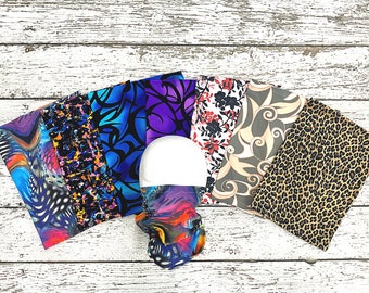 May include: A collection of eight colorful fabric swatches with various patterns, including abstract, floral, and animal prints. The swatches are arranged in a fan shape on a white wooden surface.