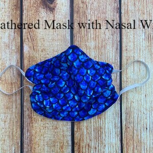 May include: A blue and white patterned face mask with white elastic ear loops. The mask has a gathered design and a wire nose piece. The text "Gathered Mask with Nasal Wire" is visible above the mask.