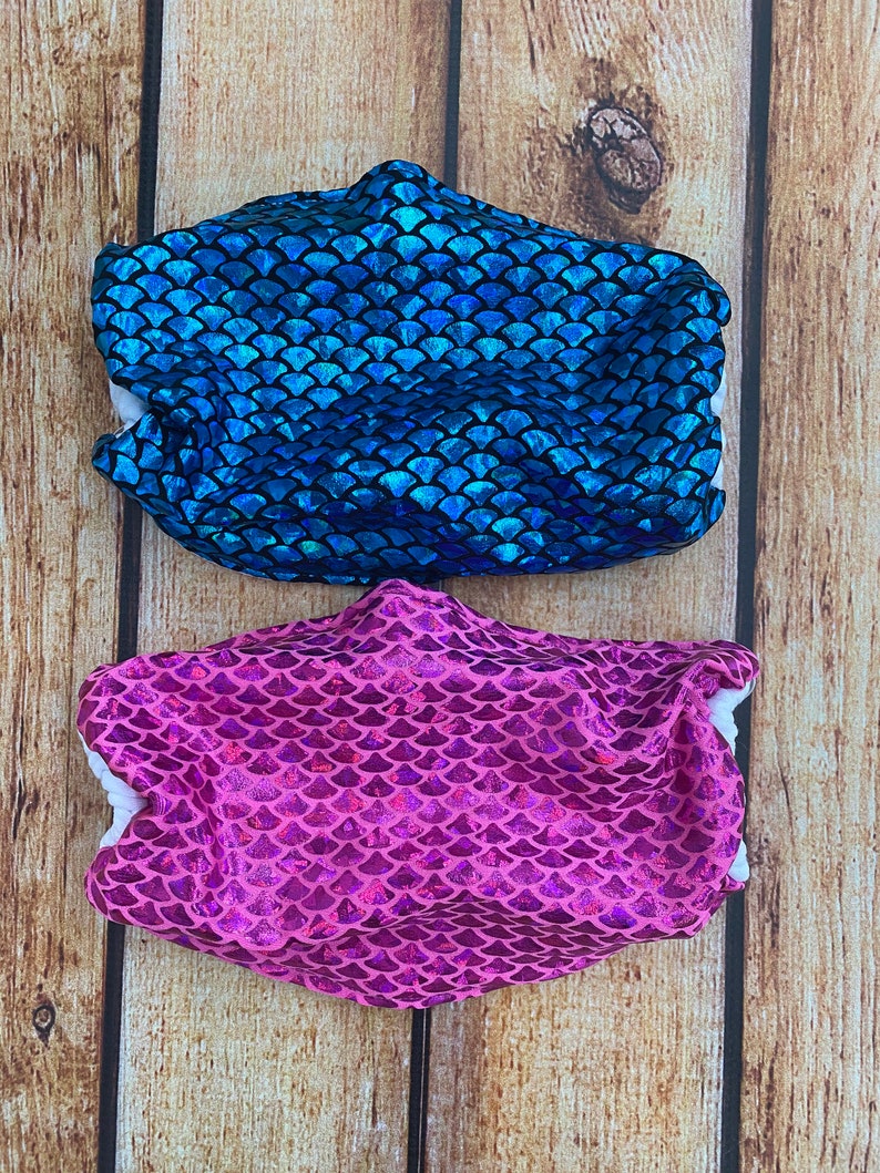 May include: Two face masks with a mermaid scale pattern. One mask is blue and the other is pink.
