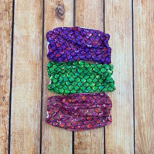 May include: Three fabric face masks with a mermaid scale pattern. The masks are purple, green, and pink.