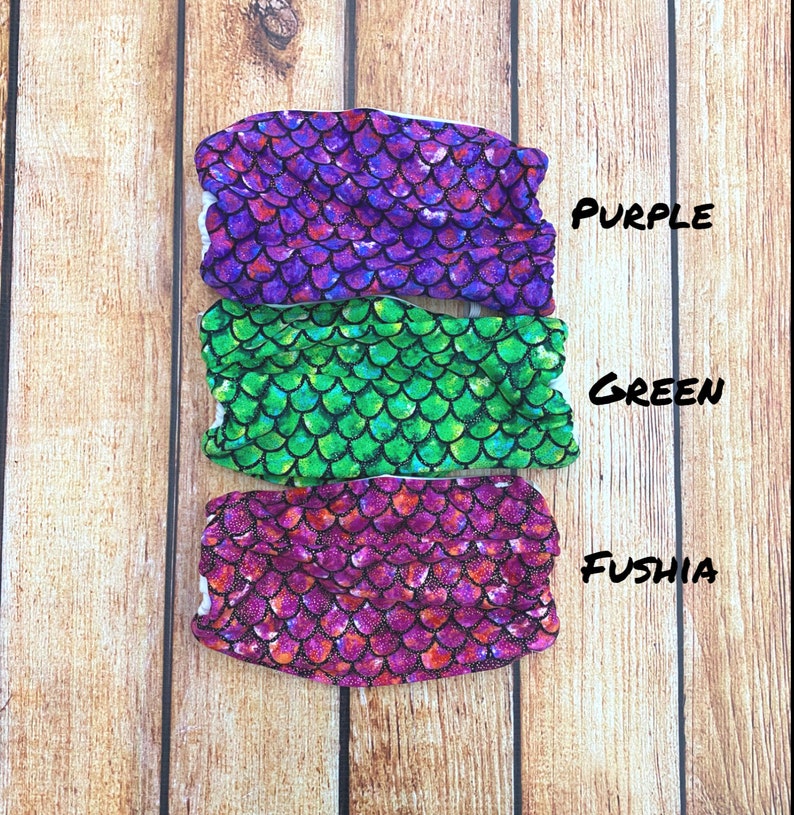 May include: Three mermaid tail fabric swatches in purple, green, and fuschia with a sparkly scale pattern. The swatches are labeled "PURPLE", "GREEN", and "FUSHIA".