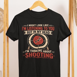 May include: Black t-shirt with a target graphic and the text "I MIGHT LOOK LIKE I'M LISTENING TO YOU BUT IN MY HEAD I'M THINKING ABOUT SHOOTING". The graphic includes a bullseye with bullet holes.