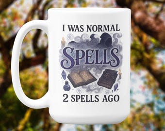 May include: White ceramic mug with a curved handle. The mug features the text "I WAS NORMAL SPELLS 2 SPELLS AGO" in a whimsical font, along with illustrations of spell books, crystals, and a hooded figure.