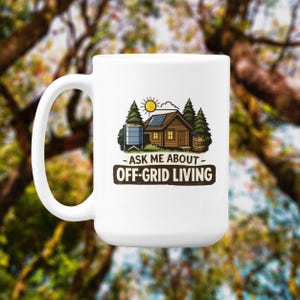 Op de afbeelding: Witte keramische mok met een hutscène, zonnepanelen, bomen en een zon. De tekst "- ASK ME ABOUT - OFF-GRID LIVING" is onder de illustratie gedrukt. De mok heeft een groot handvat. De achtergrond is wazig.