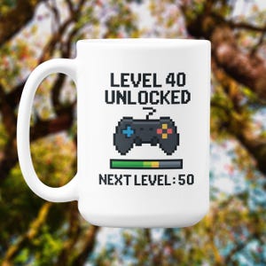 Pode incluir: Caneca de cerâmica branca com alça preta. A caneca exibe o texto "LEVEL 40 UNLOCKED" acima de um gráfico pixelizado de um controle de jogo. Abaixo, uma barra de progresso e o texto "NEXT LEVEL: 50".