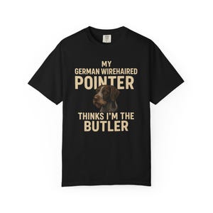Pode incluir: Camiseta preta com o texto "MY GERMAN WIREHAIRED POINTER THINKS I'M THE BUTLER" em letras bege. A camiseta apresenta um gráfico de um cão Pointer Alemão de Pelo Duro.