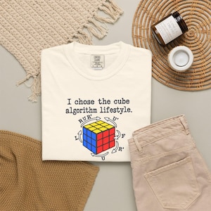 Op de afbeelding: Een crèmekleurig T-shirt met een afbeelding van een veelkleurige kubus met zwarte pijlen en de tekst "I chose the cube algorithm lifestyle." Het shirt heeft een Comfort Colors-merklabel bij de binnenhals, wat de maat large aangeeft.