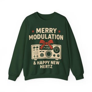 May include: Dark green sweatshirt featuring the text "MERRY MODULATION & HAPPY NEW HERTZ" in white. A vintage radio graphic is centered below the text, with a red bow. The sweatshirt is a festive holiday design.