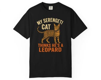 Pode incluir: Camiseta preta com um gráfico de um gato malhado e o texto "MY SERENGETI CAT THINKS HE'S A LEOPARD" em laranja e bege. O gráfico do gato é uma ilustração detalhada de um gato malhado.