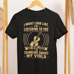 May include: Black t-shirt with a musical theme. The shirt features a graphic of a viola and text that reads "I might look like I'm listening to you, but in my head I'm thinking about my viola."