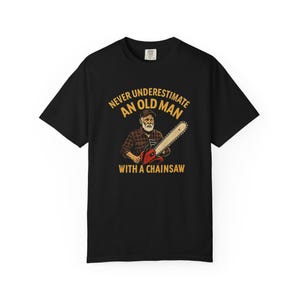 May include: Black t-shirt with a graphic of an older man holding a chainsaw. The text says "Never Underestimate an Old Man with a Chainsaw" in yellow and white. The design includes a red and silver chainsaw.