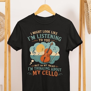 May include: Black t-shirt with the text "I might look like I'm listening to you, but in my head I'm thinking about my cello." The graphic features a cello, musical notes, and a sun.