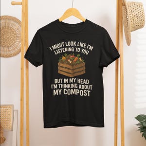 May include: Black t-shirt with the text "I MIGHT LOOK LIKE I'M LISTENING TO YOU BUT IN MY HEAD I'M THINKING ABOUT MY COMPOST". The shirt features a graphic of a compost bin with vegetables.