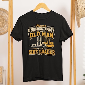 May include: A black short-sleeved t-shirt featuring a yellow and white graphic of a side loader forklift. The text reads: Never underestimate an old man with a side loader. The design is centered on the chest of the garment, which has a crew neckline.