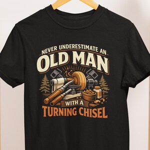 May include: Black t-shirt with a graphic design featuring the text "NEVER UNDERESTIMATE AN OLD MAN WITH A TURNING CHISEL." The design includes images of woodworking tools and a wood turning project.