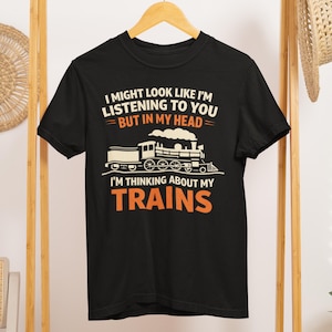 May include: Black t-shirt with a train graphic and the text "I MIGHT LOOK LIKE I'M LISTENING TO YOU BUT IN MY HEAD I'M THINKING ABOUT MY TRAINS" in white and orange. The graphic features a steam train.