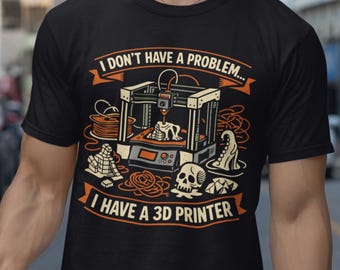 May include: A black short-sleeved t-shirt featuring a graphic of a 3D printer surrounded by printed objects like a skull and tentacle. The text reads, "I DON'T HAVE A PROBLEM... I HAVE A 3D PRINTER" in orange and white lettering.