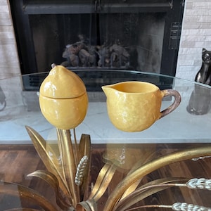 May include: A yellow ceramic lidded sugar bowl and a matching yellow creamer pitcher with a brown handle. Both pieces feature a textured, glossy finish and rounded, organic shapes. The sugar bowl has a small pointed lid, while the creamer has a spout.