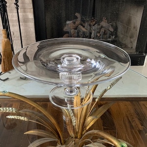 May include: A clear glass cake stand with a round top and a pedestal base. The stand is made of clear glass and has a simple, elegant design. The stand is perfect for displaying cakes, cupcakes, or other desserts.