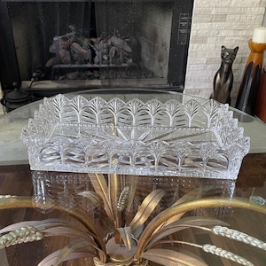 May include: A rectangular clear glass tray featuring a decorative scalloped edge with a leaf-like pattern and a starburst design etched into the base. The tray has vertical sides with a repeating pointed arch motif and a smooth, flat interior surface.