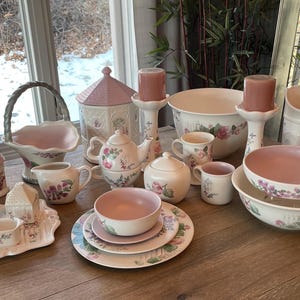 May include: A collection of vintage-style teacups, saucers, and other tableware featuring a floral pattern with pink and green accents. The set includes a teapot, sugar bowl, creamer, and a variety of cups and saucers.