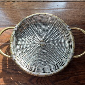 May include: A silver and gold woven wicker basket with two handles. The basket is round and has a woven pattern.
