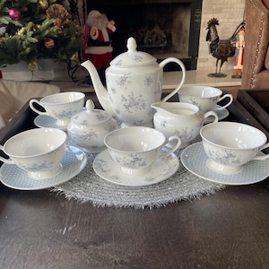 May include: A white tea set with a floral pattern. The set includes a teapot, creamer, sugar bowl, and four teacups and saucers.