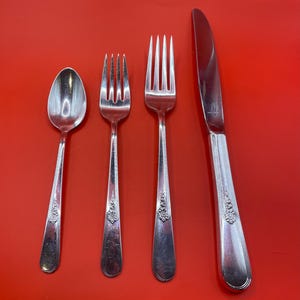 May include: A set of four silver-plated flatware pieces, including a knife, fork, and two spoons, on a red background.