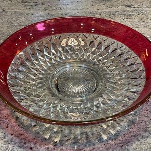 May include: A clear glass bowl with a diamond pattern and a red rim. The bowl is perfect for serving fruit, snacks, or salads.