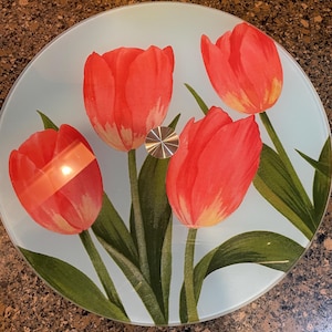 May include: A round glass table top with a design of four red tulips with green leaves on a light blue background.