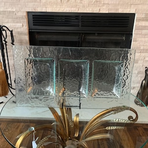 May include: A clear, rectangular glass serving dish with three square compartments. The glass has a textured, bubbly surface. The dish sits on a glass table with a gold-colored decorative base.
