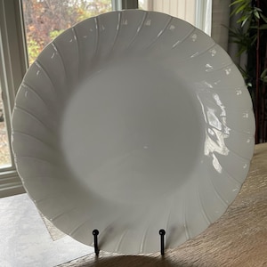 May include: White ceramic dinner plate with a swirl design. The plate is on a black metal stand.