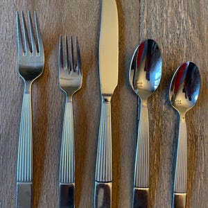 May include: Set of five silver-toned flatware pieces with a ridged design on the handles. The set includes a knife, fork, and three spoons.
