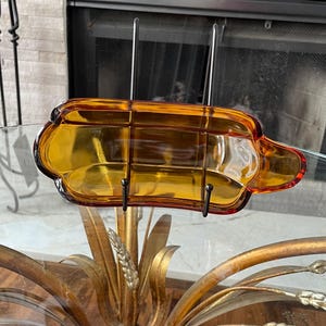 May include: Amber-colored glass serving dish with a rectangular shape and a handle on one side. The dish is divided into sections and sits on a glass table. The dish is likely used for serving snacks or appetizers.