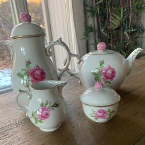 May include: A white porcelain tea set with a pink rose design. The set includes a teapot, creamer, sugar bowl, and coffee pot.