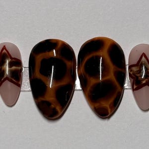 May include: Set of ten false nails with different designs.  The designs include a red and white star, a cherry, a leopard print, and a brown and red geometric pattern.